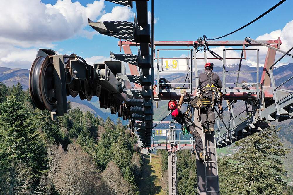 Photo aérienne prise par Joël Estrade, photographe et pilote de drone basé dans les Pyrénées centrales, spécialisé dans le reportage industriel. Cette image montre, dans le cadre d'un suivi d'un chantier d'installation de télécabine, 2 techniciens qui s'occupent du démontage d'un ancien pylône.