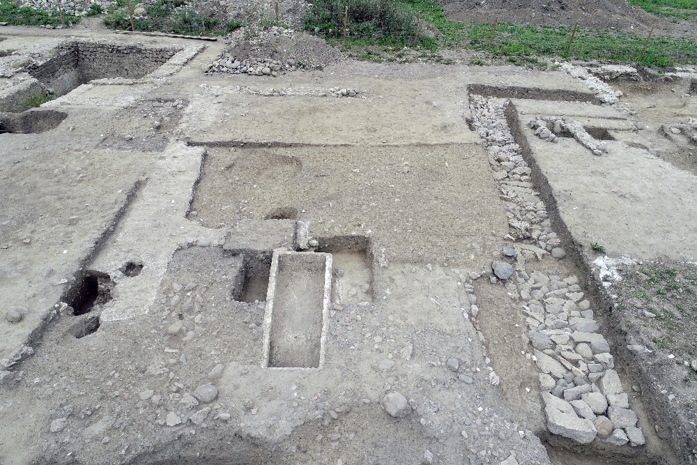 Cette image représente une vue aérienne d'un chantier de fouilles archéologiques. On voit bien les fondations de certains monuments et des traces de sépultures, dont un sarcophage intact